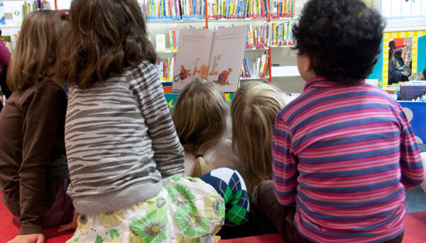 Kinder sitzen im Kreis um eine Frau und blicken interessiert auf das Buch, das sie zeigt